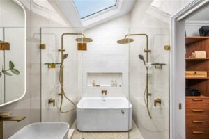 Blog - Skylight on a raked ceiling above a freestanding bath flanked by twin brass shower heads in a luxury bathroom
