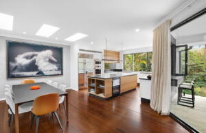 Blog - Row of three flat skylights above an open-plan kitchen and dining room with timber flooring and statement wave artwork