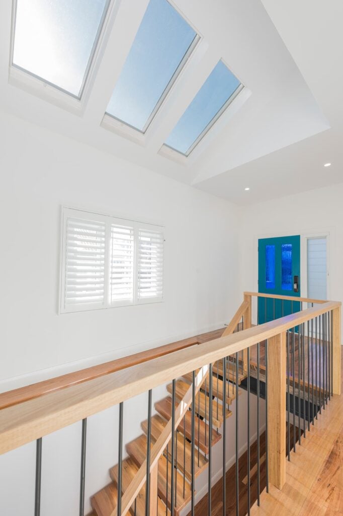 Multiple skylights above a timber staircase landing with a striking blue front door entry