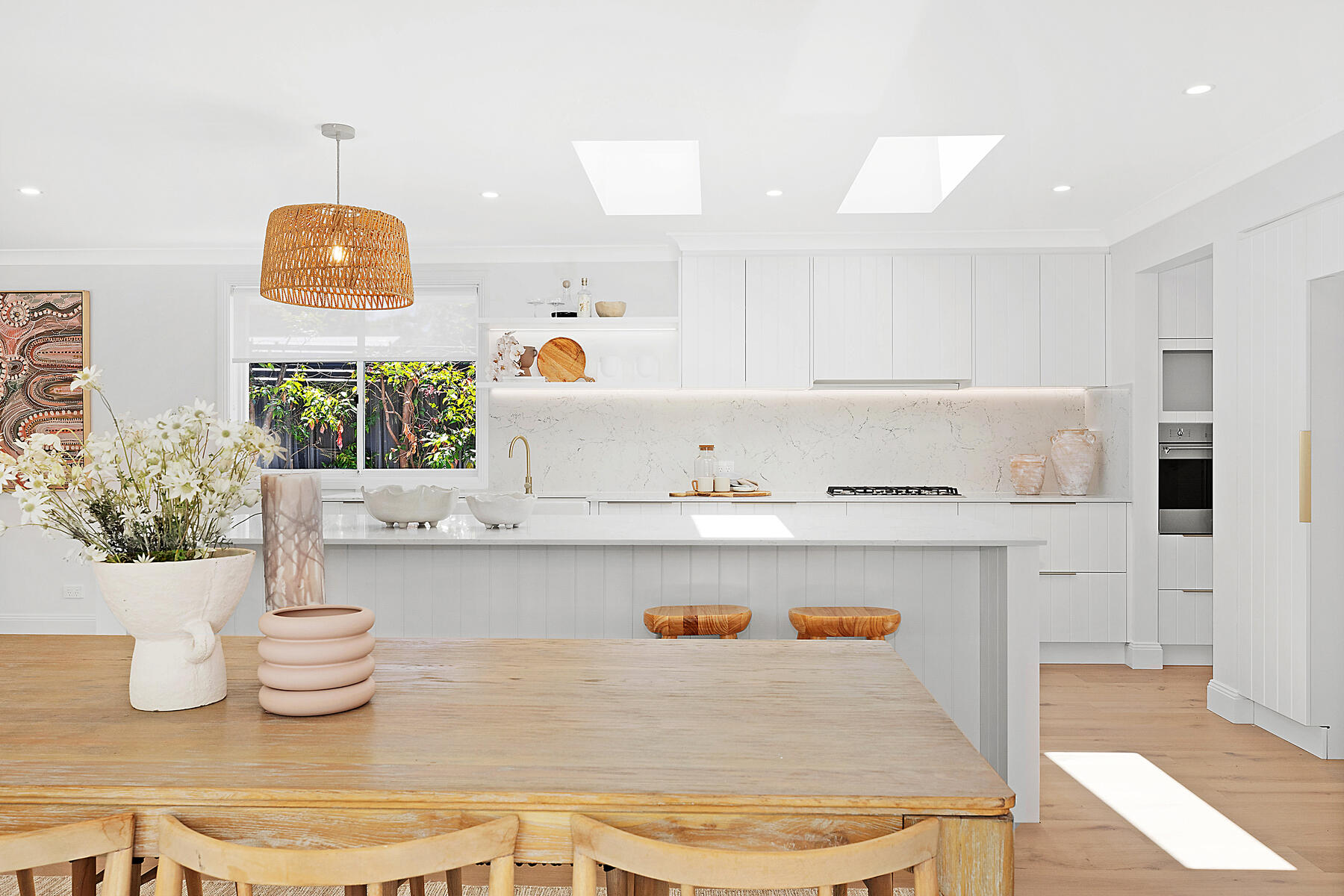 Modern coastal kitchen renovation in Lake Macquarie featuring twin skylights, white cabinetry, an engineered stone island bench, and natural timber dining finishes.